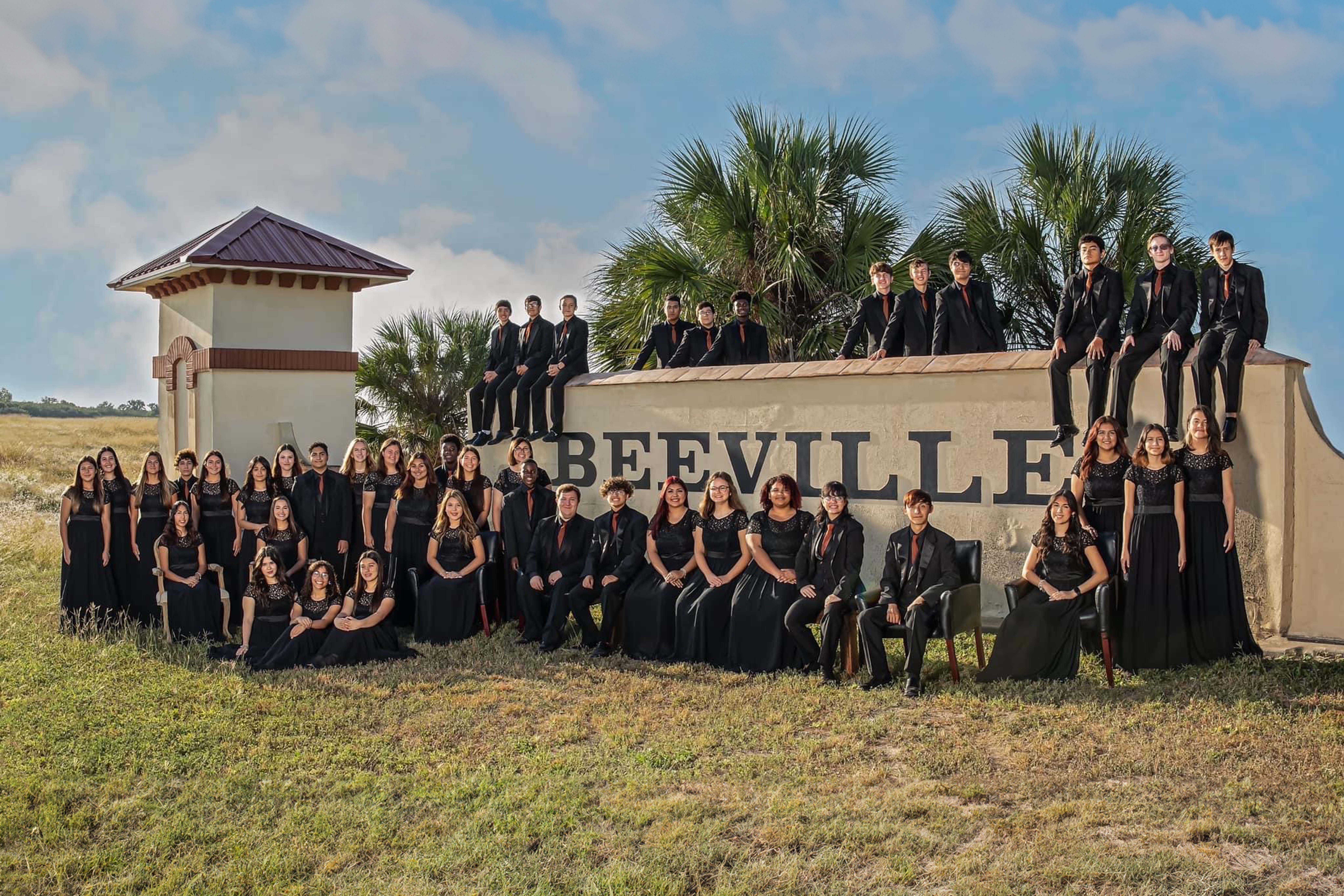the beeville high school choir is all dressed up and taking a group picture in front of city's stone sign